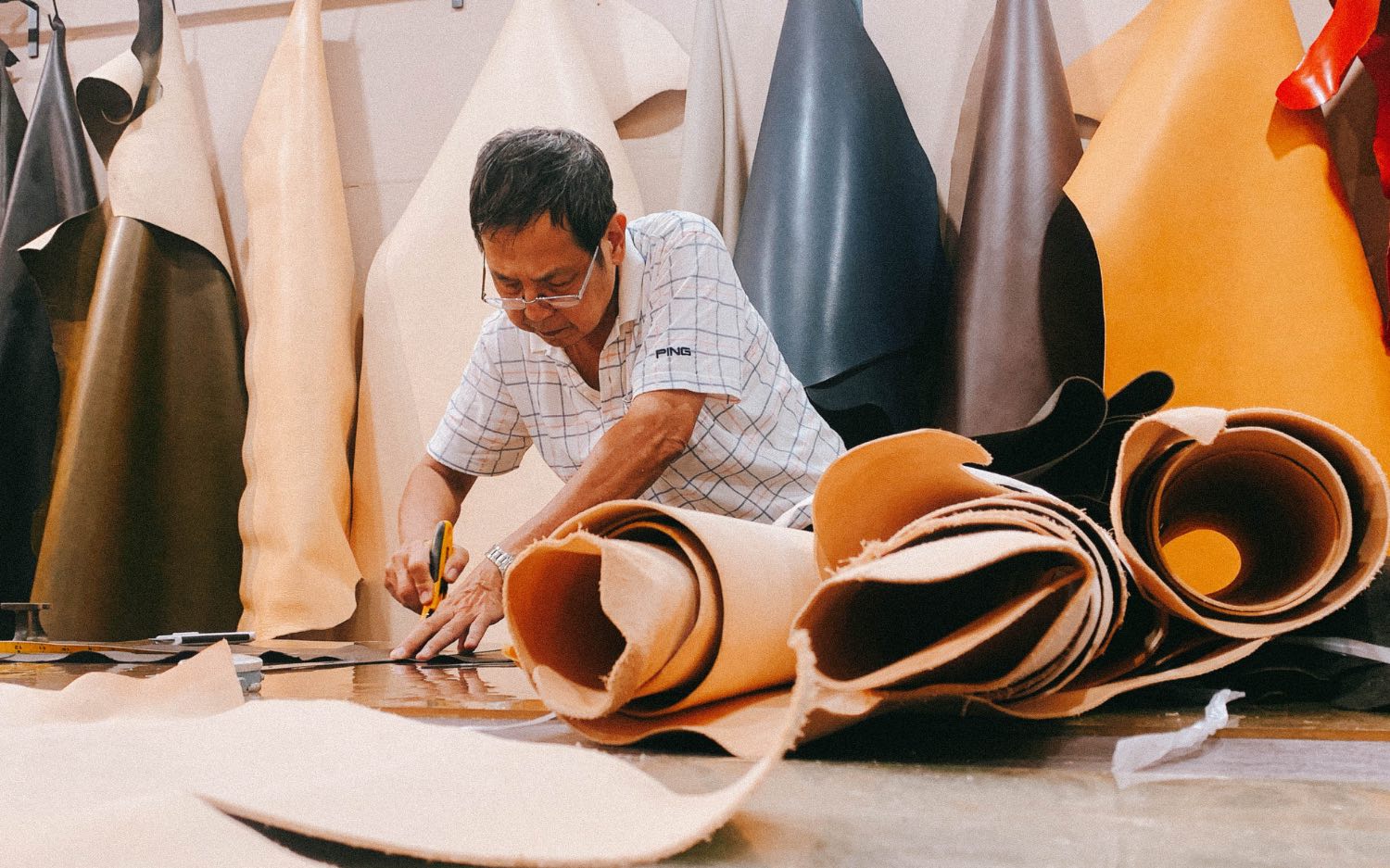 An artisan cutting leather at the material rack — an everyday scene in the workshop