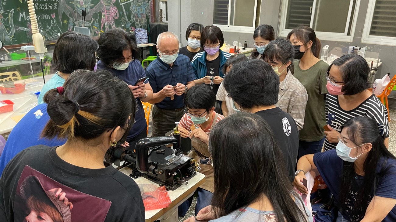 An instructor demonstrating a sewing machine while students gather around