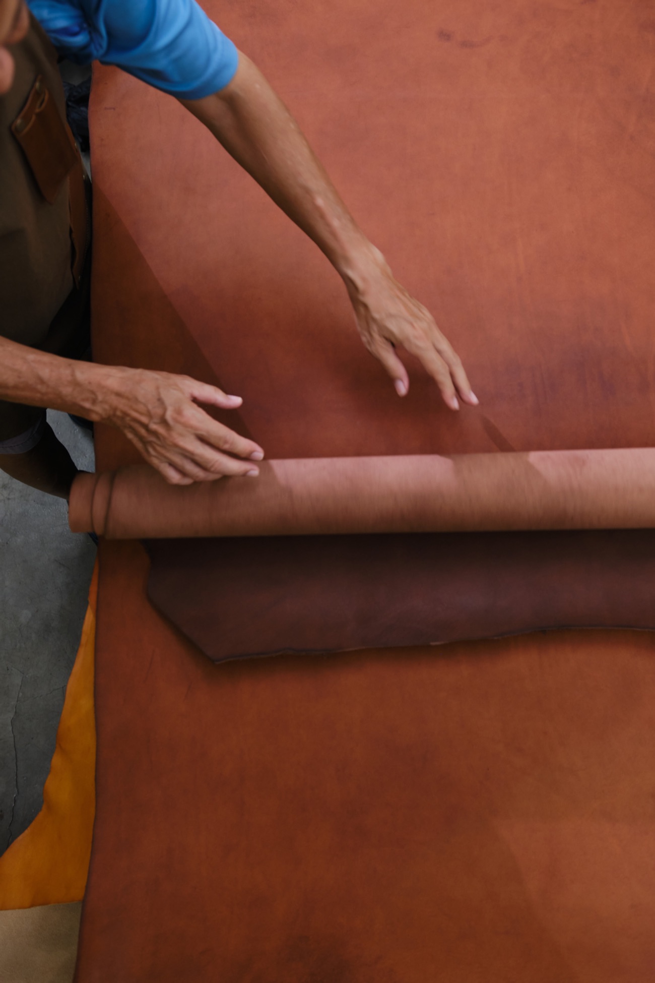 An SG Leather artisan sorting a roll of vegetable-tanned leather at the workbench, checking its grain