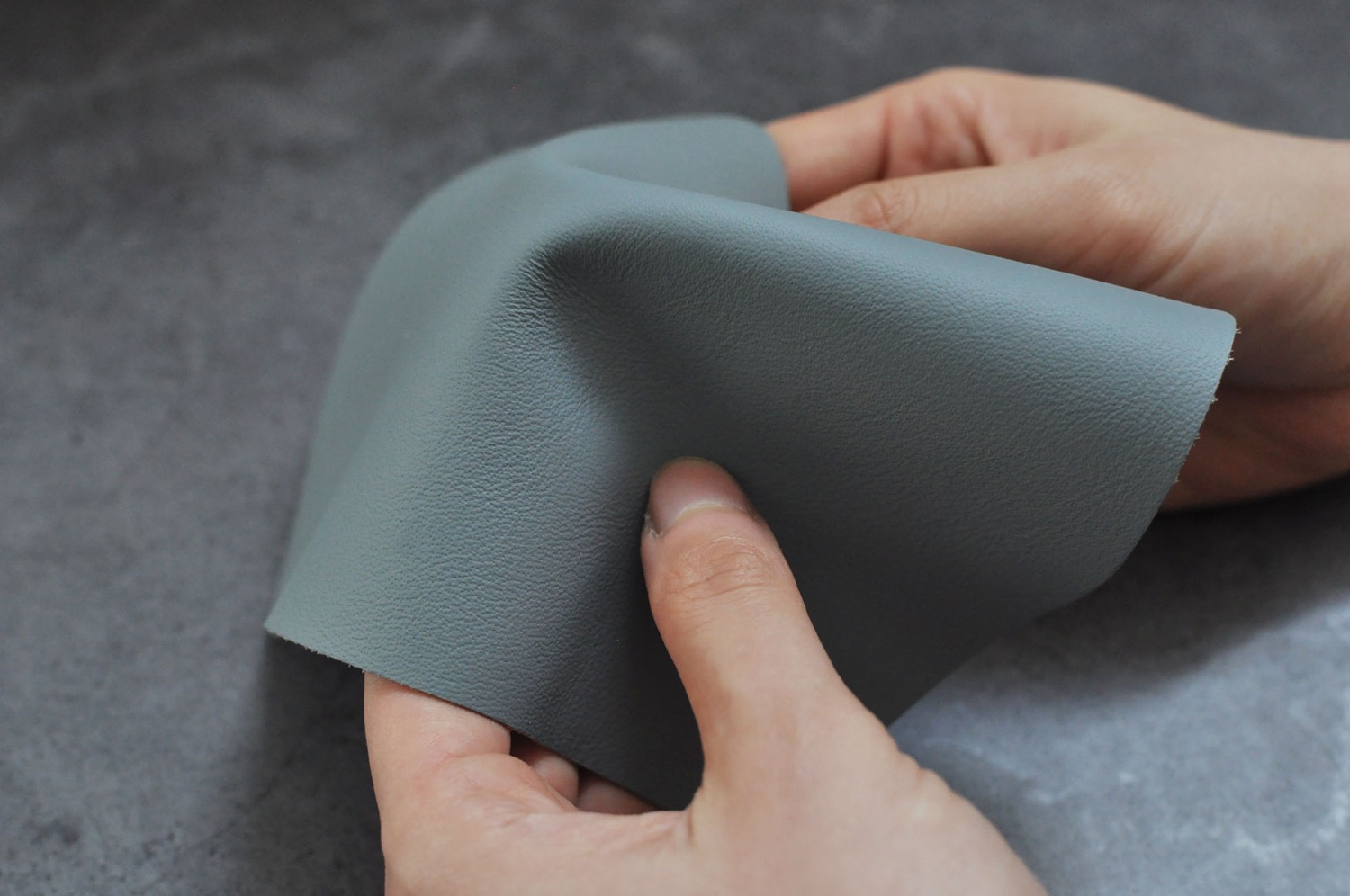Close-up of chrome-tanned leather, a soft gray hide folded in hand, fine and supple