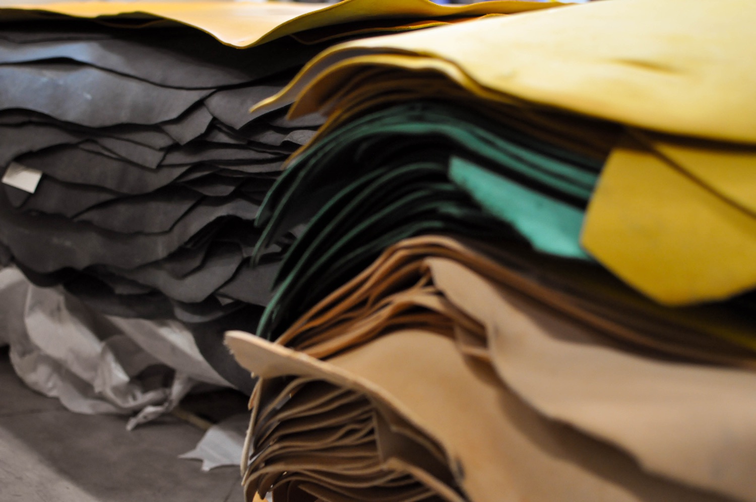Rolls of leather in many colors stacked at SG Leather — yellow, dark green, tan and gray, both vegetable- and chrome-tanned