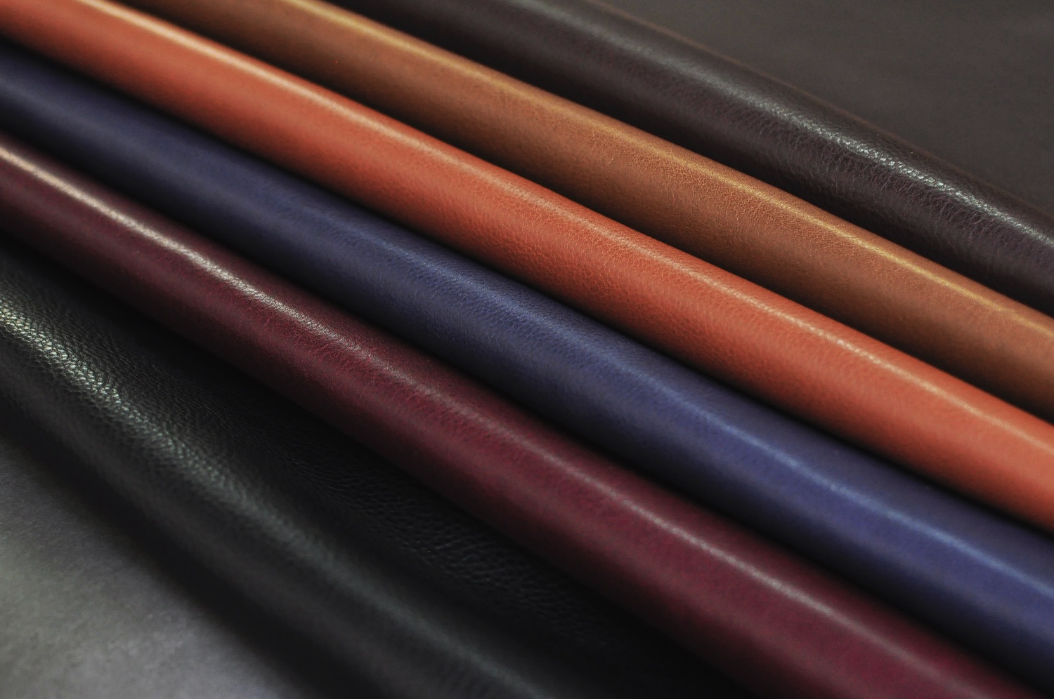 Close-up of vegetable-tanned leather rolls in red, blue, brown and black, with natural grain and saturated color