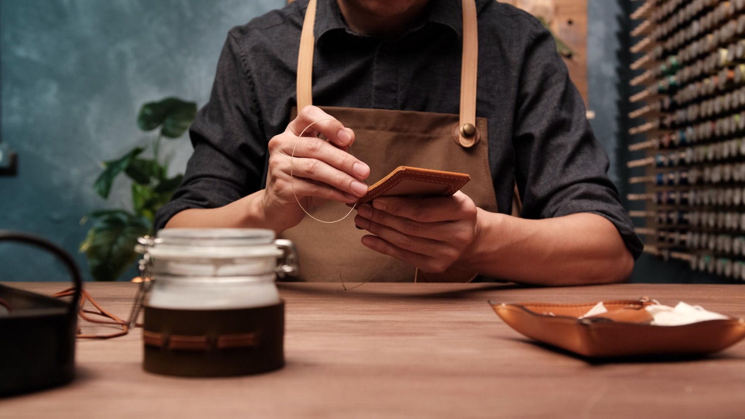 A leather artisan hand-stitching a wallet in the workshop during a class