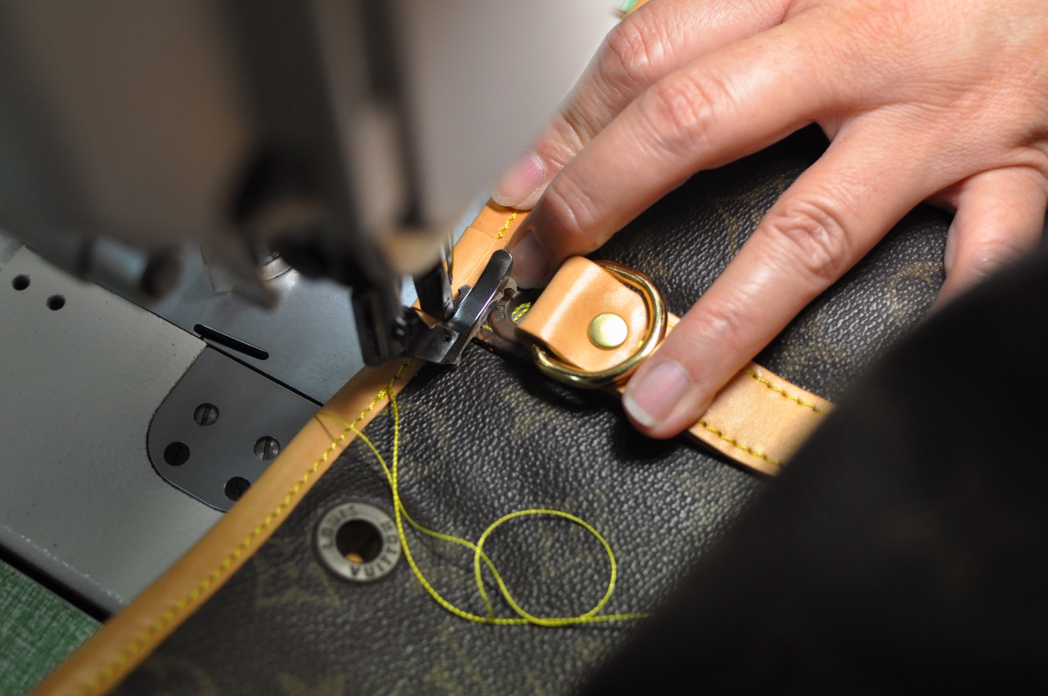 An artisan repairing a designer bag's leather handle and hardware on a sewing machine