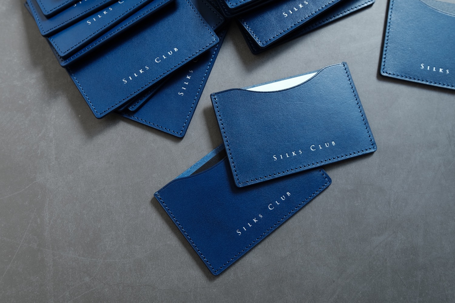 A navy leather card holder embossed with a brand name, an example of leather brand manufacturing